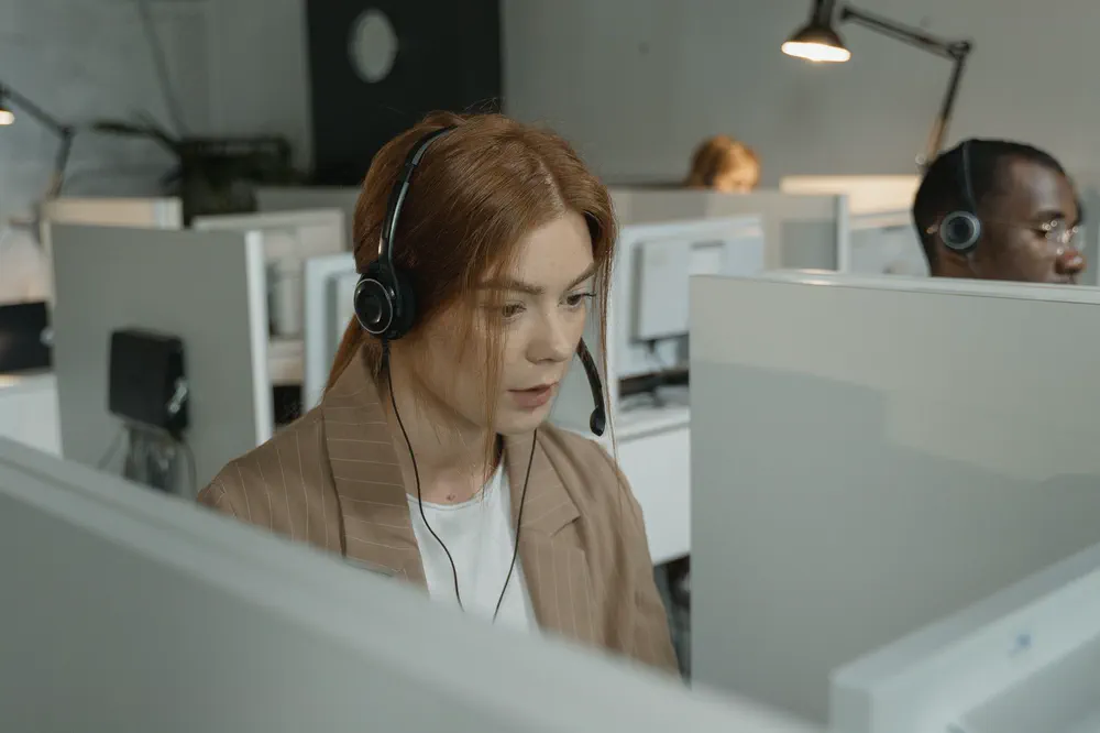 Une télésecrétaire, casque sur les oreilles, au travail devant son écran dans un grand bureau partagé.