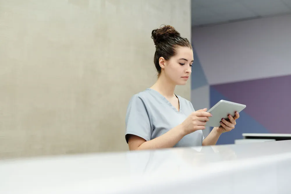 Accueil d’un cabinet médical : une secrétaire consulte une tablette au comptoir de réception.