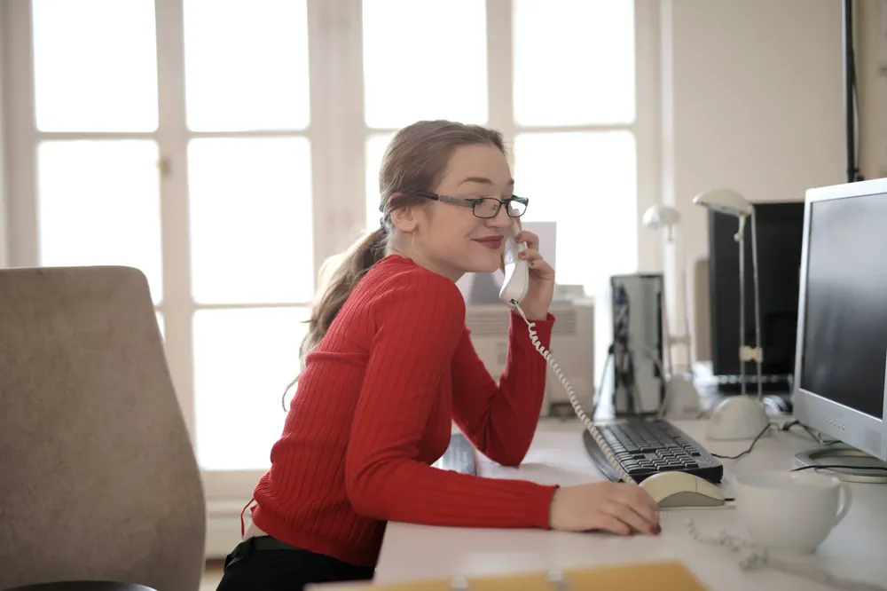 Une secrétaire répond au téléphone à son poste de travail, devant son ordinateur.