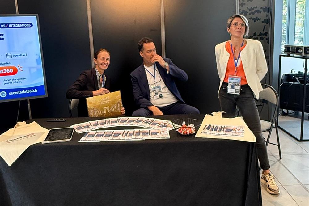 Le stand Secretariat360 au salon CSMF 2026 : trois personnes derrière une table couverte de brochures et de sacs.